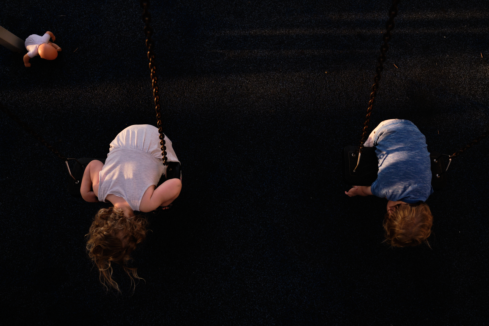 צילום של שני ילדים תלויים על נדנדות עם בובה ליד בתנוחה דומה